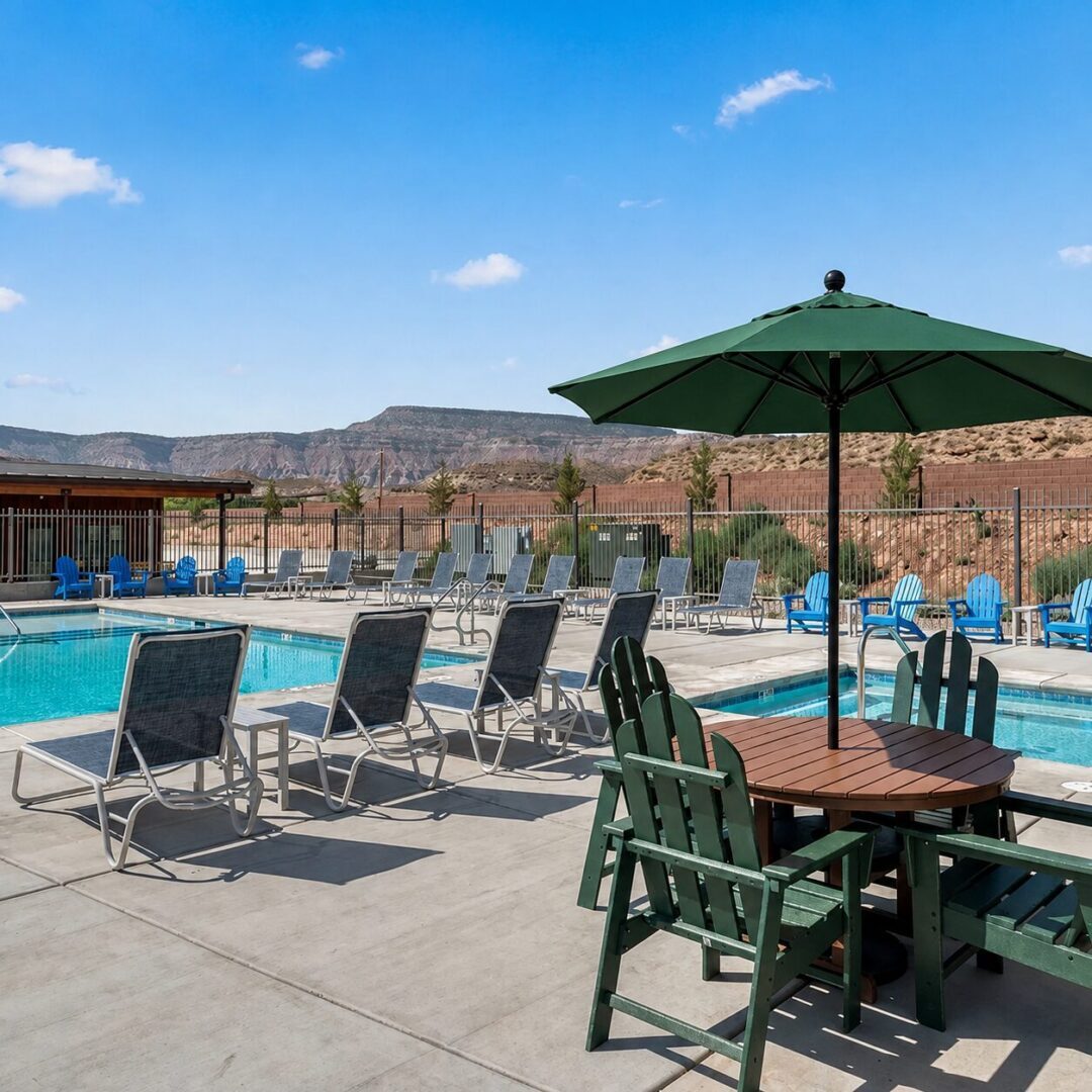 Poolside chairs and table under green umbrella.
